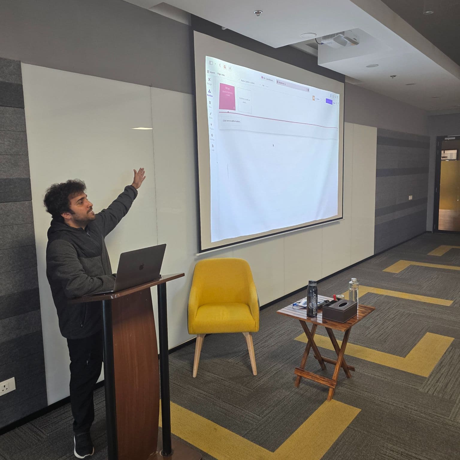 Adi presenting on stage in front of a projected slide.